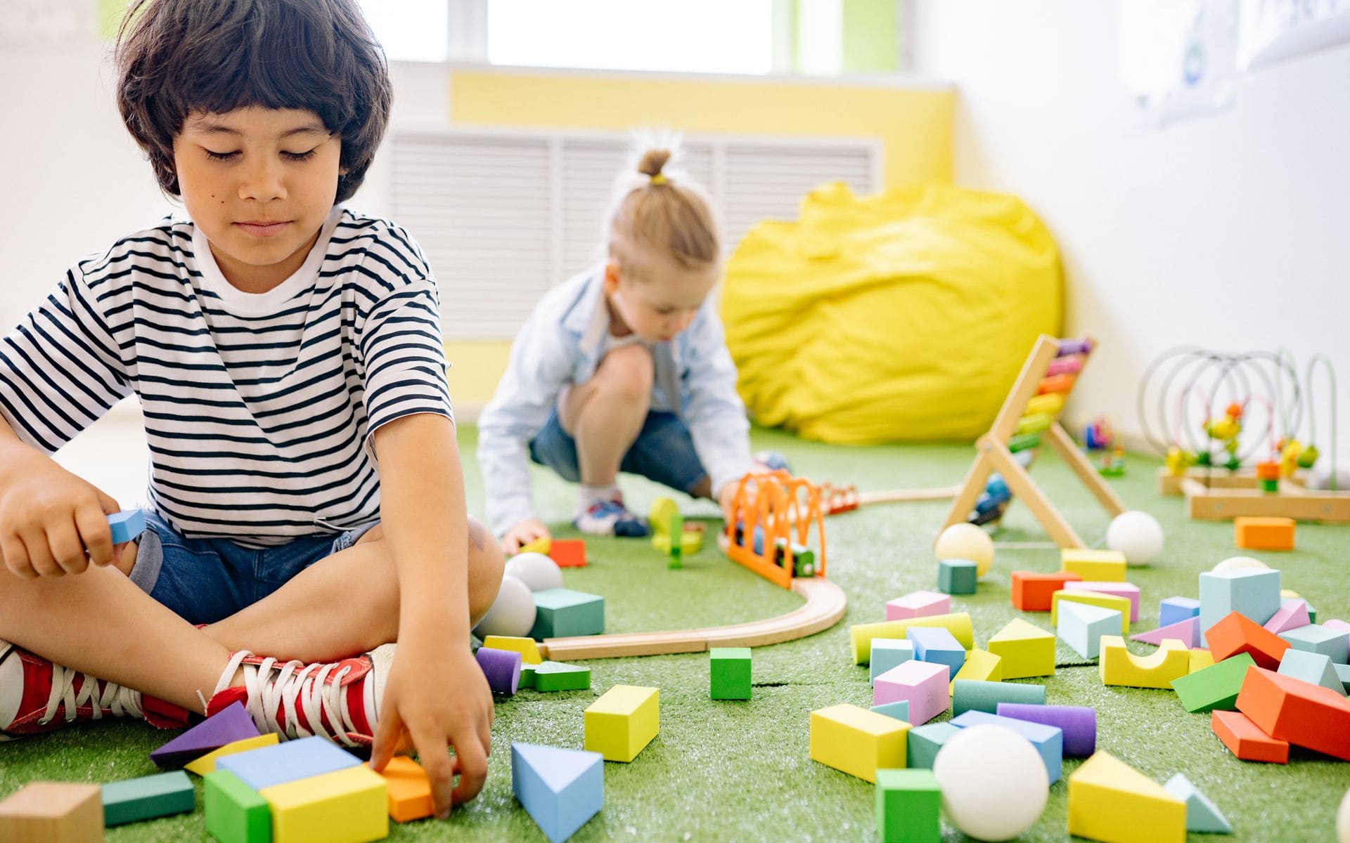 Two children playing with colourful building blocks in a bright playroom