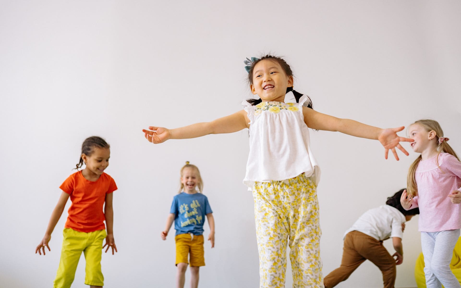 Several small children of different backgrounds playing and jumping together in a bright room