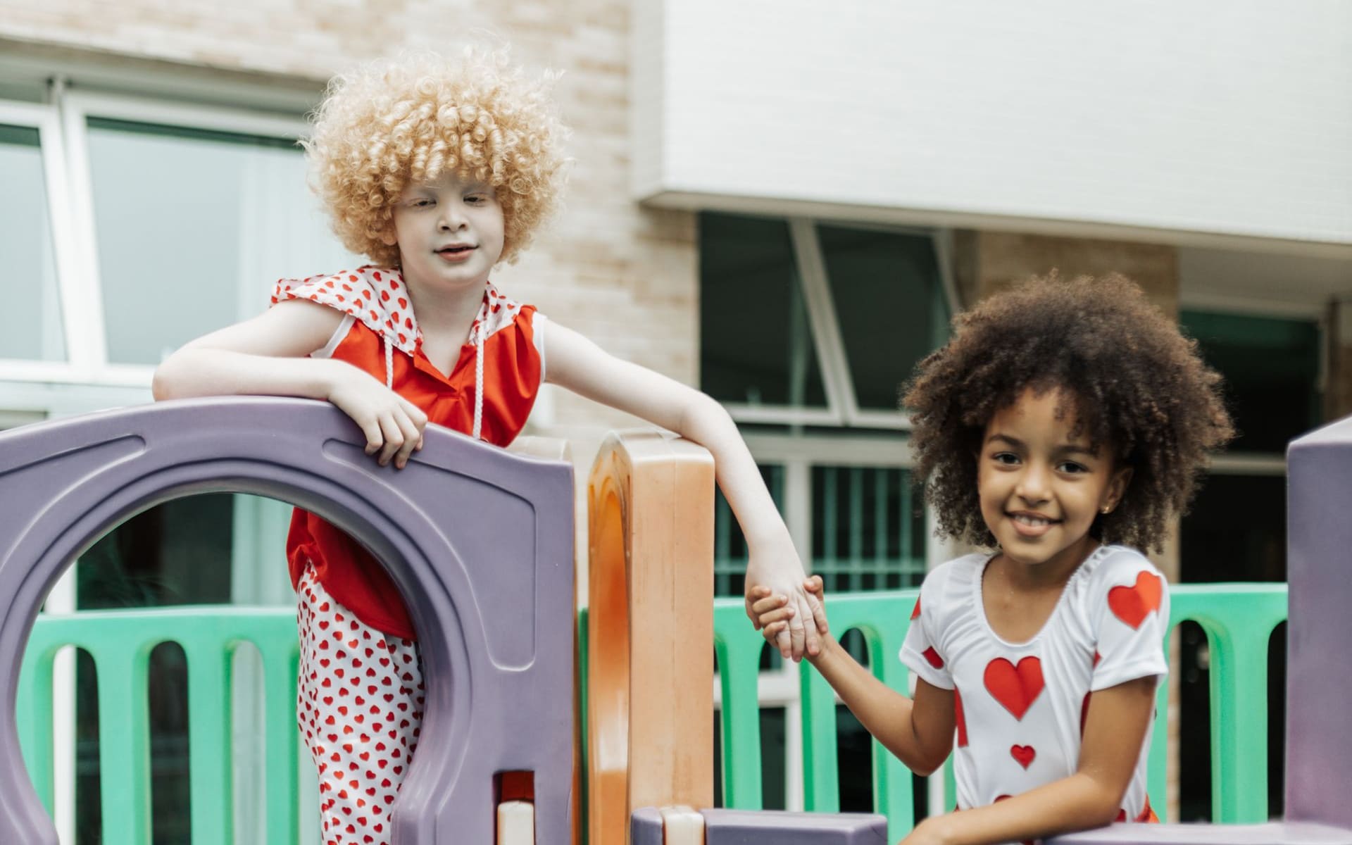 Two children of different backgrounds holding hands and helping each other on a playground